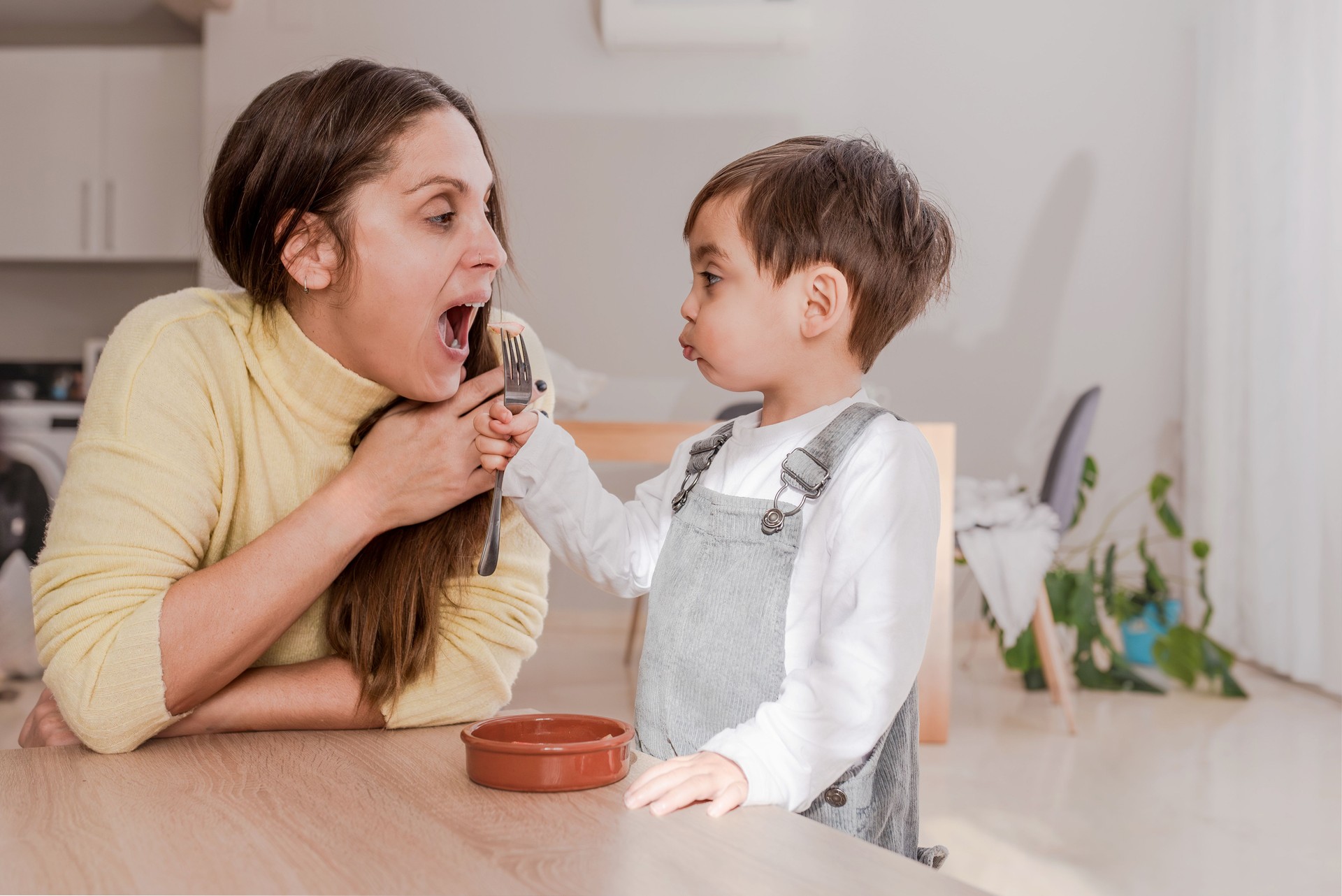Mother Playing Airplane with Spoon During Mealtime with Her Young Son at home